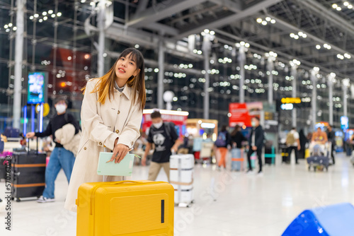 Attractive Asian woman holding passport and luggage walking to airline check in counter in airport terminal. People travel on airplane on holiday vacation and global airline transportation concept.