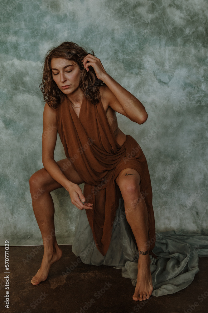 Naklejka premium portrait of a non-binary person sitting on a box leaning forward tucking hair behind ear