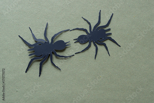 two black paper spider glyph dingbat cutouts on rough green paper