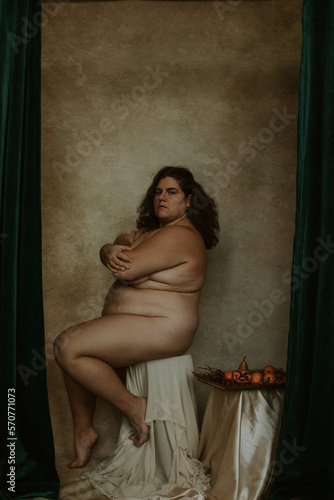 portrait of a plus size woman sitting on a stool next to a plate of fruit against textured backdrop