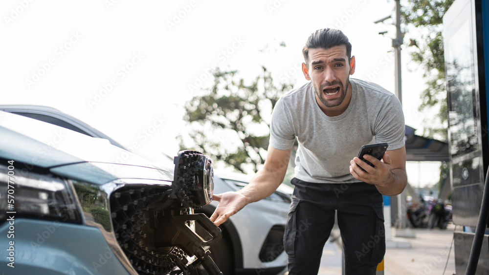 Young man outside car. Dissapointed businessman talking on phone. Broken car charger problem stand besides. Helpless user need help and assistance. Electric car accident. Car trouble