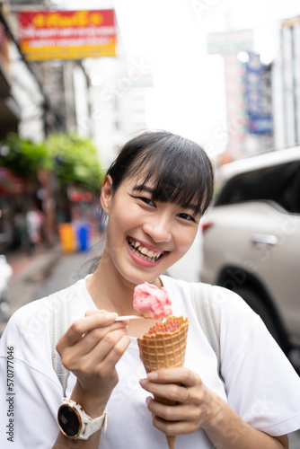 Young Asian student female eating iced cream  while holiday alone. Happy woman enjoying street food in the city holidays concept.