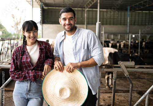 Portrait of couple multi racial diversity Asian and Hispanic farmers who are standing at the cow farm.