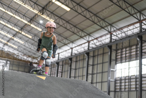 asian child skater or kid girl fun playing skateboard or ride surf skate to start on wave ramp pump track in skate park by extreme sports surfing to wear helmet elbow wrist knee guard for body safety © kornnphoto