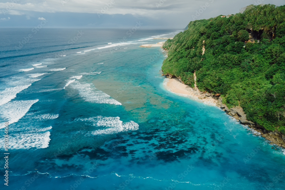 Aerial view of coastline with turquoise ocean and tropical beach under cliffs in Bali.