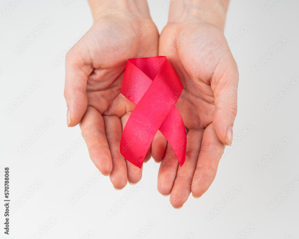 Female hands with a red ribbon on a white background. Symbol of the fight against AIDS. Female hands with a red ribbon on a white background. Symbol of the fight against AIDS.