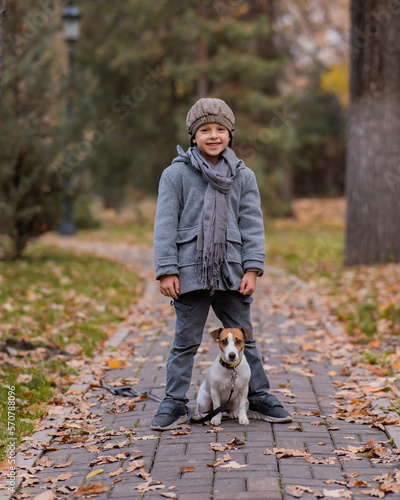 Caucasian boy walking with dog jack russell terrier in autumn park.