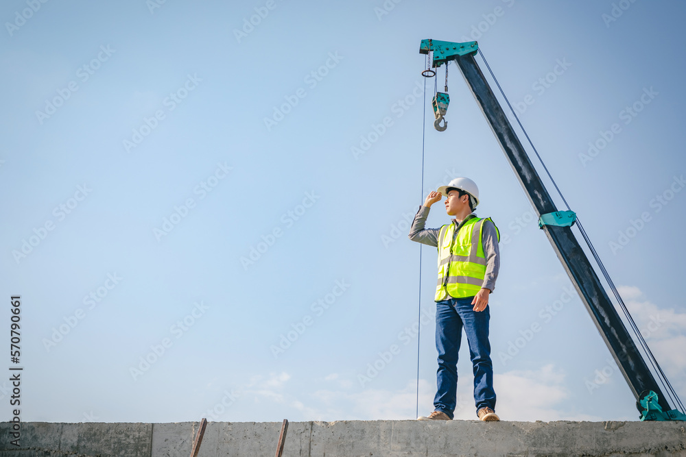 Successful Worker Wearing Hard Hat and Safety Vest Standing on  Building Construction Site Crane Machinery  and blue sky Background,