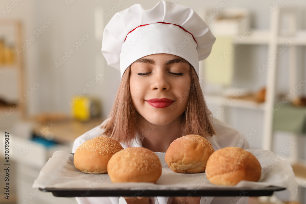 Female baker with tray of tasty buns in kitchen, closeup Female baker with tray of tasty buns in kitchen, closeup