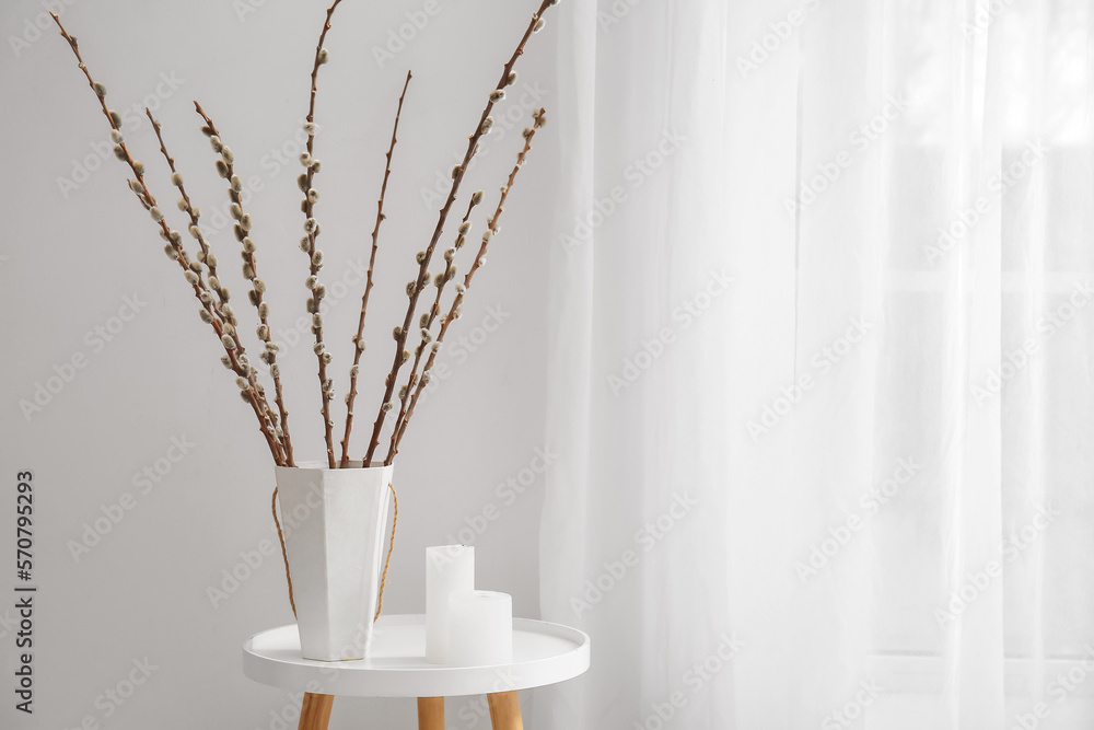 Vase with willow branches and candles on table near light curtain