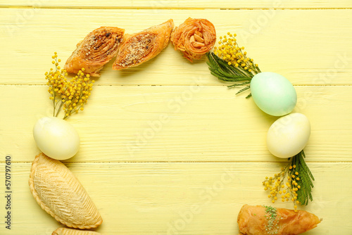 Frame made of flowers, eggs and treats on yellow wooden background. Novruz Bayram celebration