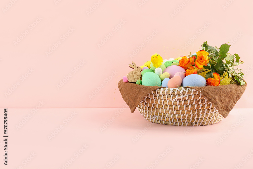 Wicker basket with Easter eggs, decor and flowers on color background
