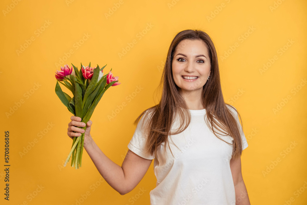 Happy young girl with a bouquet of flowers on a yellow background, holiday concept, woman day