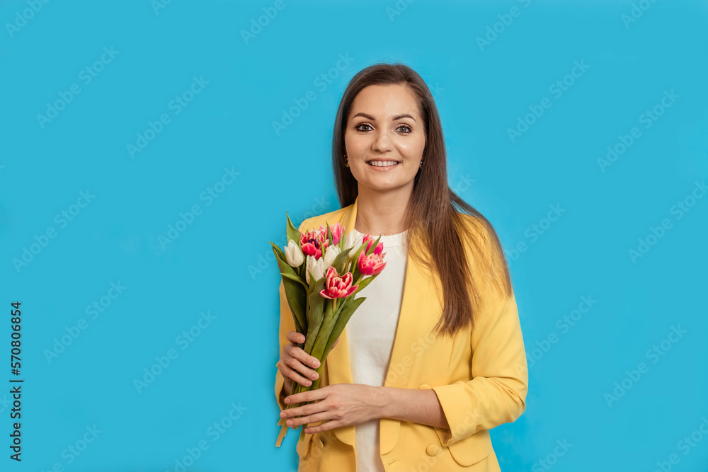 Portrait of a happy young woman in a yellow jacket on a blue background with a bouquet of flowers Portrait of a happy young woman in a yellow jacket on a blue background with a bouquet of flowers