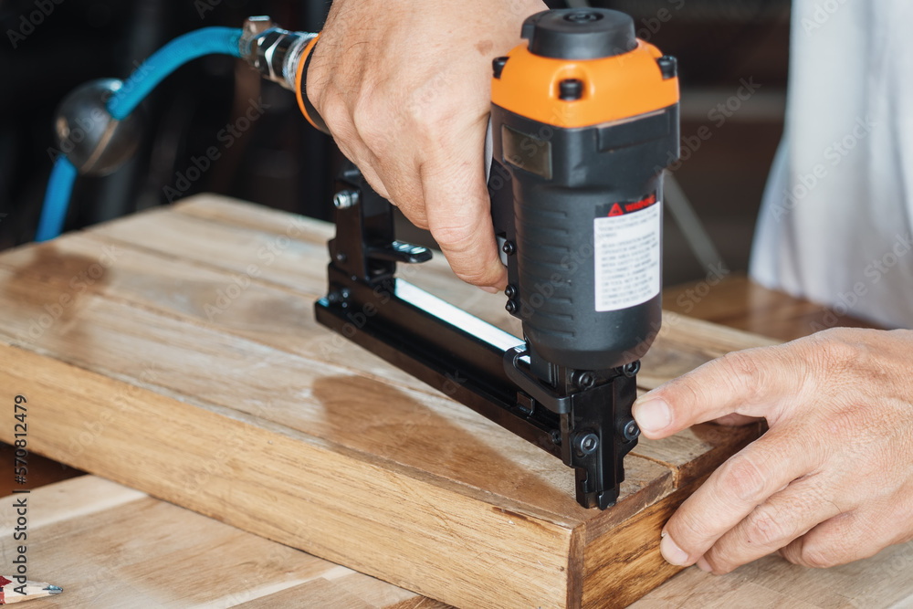 carpenter using nail gun or brad nailer tool on wood box in a workshop ,furniture restoration woodworking concept. selective focus carpenter using nail gun or brad nailer tool on wood box in a workshop ,furniture restoration woodworking concept. selective focus