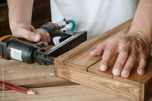 Photos carpenter using nail gun or brad nailer tool on wood box in a workshop ,furniture restoration woodworking concept