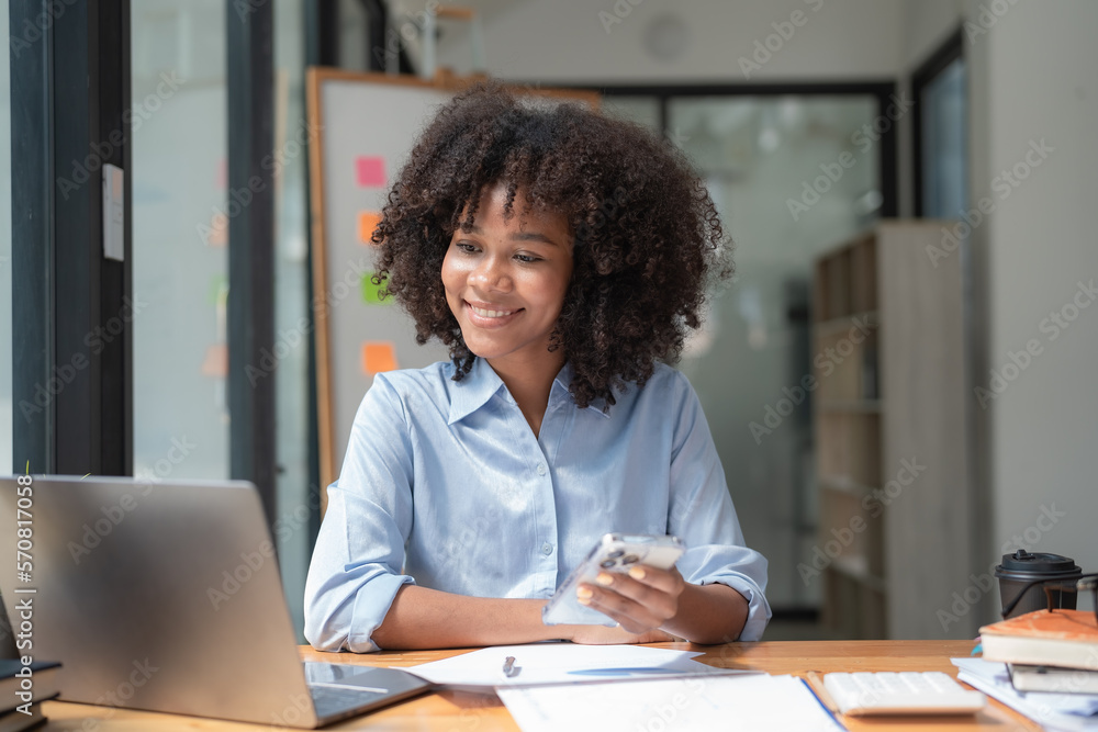 Smiling African American businesswoman working on a laptop sitting at her desk in a modern office. Smiling African American businesswoman working on a laptop sitting at her desk in a modern office.
