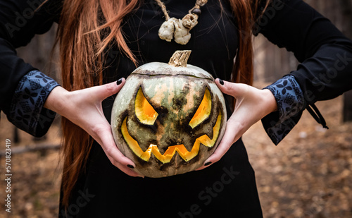 A red-haired girl holding a pumpkin in celebration of Halloween against a backdrop of an autumnal forest.