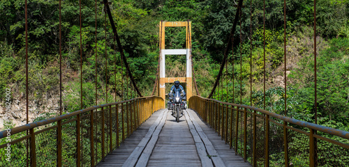 Man driving touring motorbike on suspension bridge in Peru
