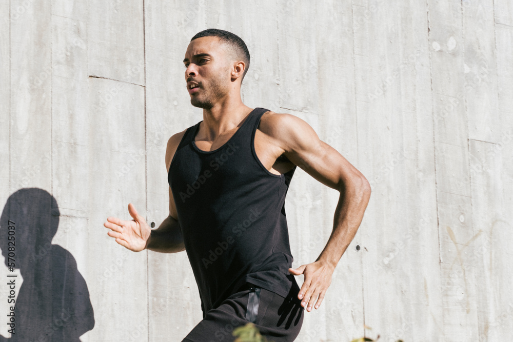 Upper part African American male athlete running against concrete wall Upper part African American male athlete running against concrete wall