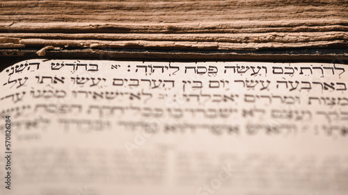Page of old worn shabby jewish book Torah. Selective focus on snippet Hebrew Bible text that translates in english: offer the Passover sacrifice to Jehovah. Korban Pesach. Closeup. photo