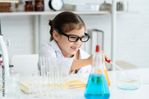 Adorable Asian girl sits in science class, happy faces studying in science class, practical class, squeezing water from flask into beaker, slowly doing experiment and waiting to see results.