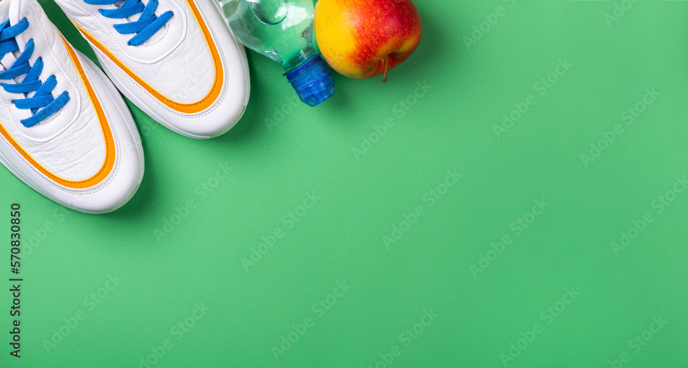 Sport shoes and sport equipment for fitness healthy lifestyle, exercise, healthy food concept. Sport background with shoes, fruit and water bottle on green. Copy space
