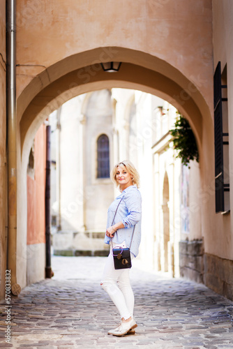 blonde woman in a blue shirt and light pants walks a summer town