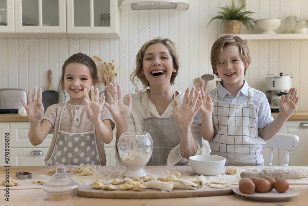 Happy mother and kids baking in kitchen portrait. Cheerful mom, little boy and girl preparing bakery food at table with dough, showing floury palms at camera, smiling, laughing, having fun Happy mother and kids baking in kitchen portrait. Cheerful mom, little boy and girl preparing bakery food at table with dough, showing floury palms at camera, smiling, laughing, having fun