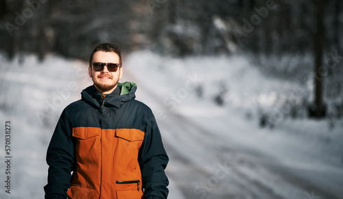 Bearded man in the winter forest. Guy wearing sunglasses during snowy weather.