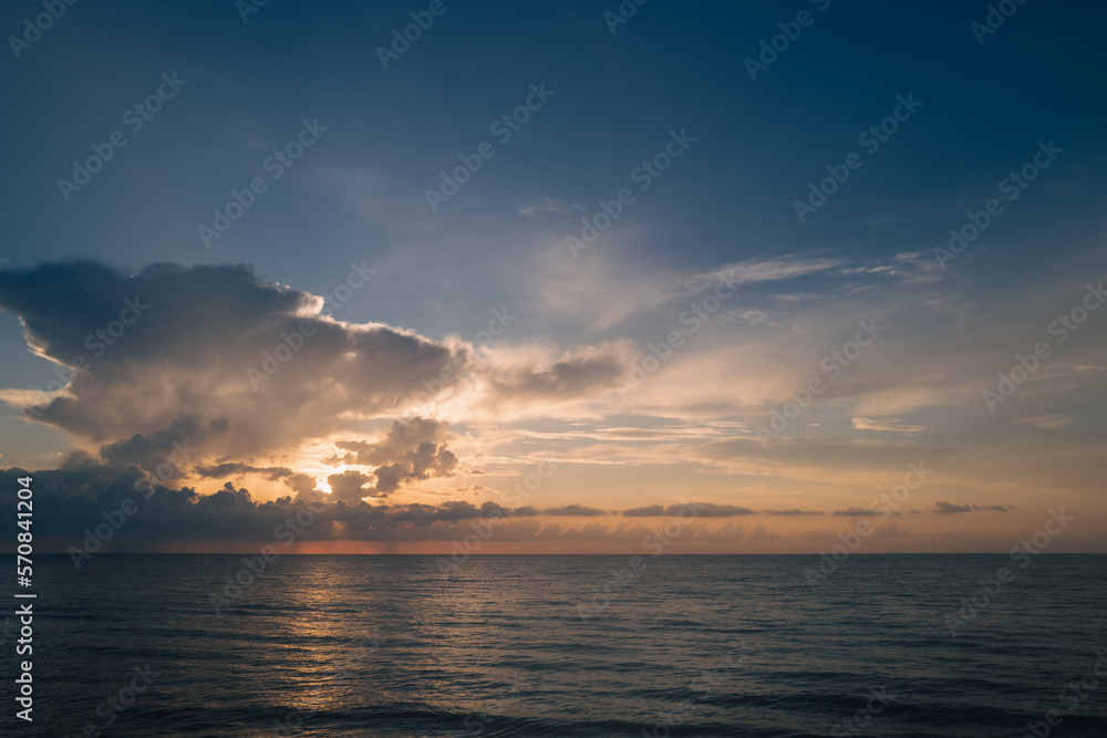 Calm sea with sunset sky and sun through the clouds over. Sunrise sea on tropical beach. Landscape of beautiful beach. Beautiful sunset at sea. Ocean sunset on sky background with colorful clouds.