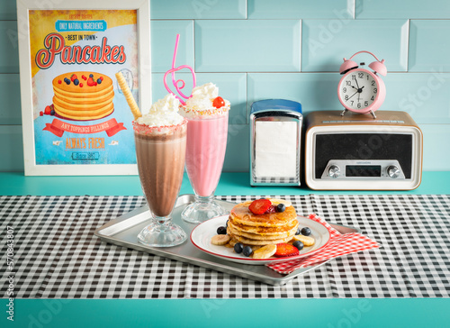 Breakfast of pancakes with fruits, a chocolate milkshake and a strawberry milkshake in vintage 1950s diner photo