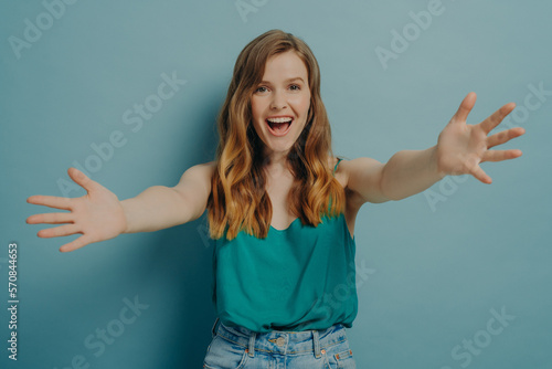 Joyful excited woman spreads her arms wide to hug someone loved, isolated on blue background