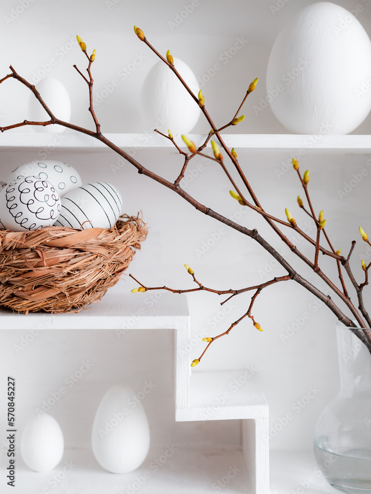 Home minimalist interior with Easter decor. Branches with budding buds in a glass vase on shelves in the shape of a house,