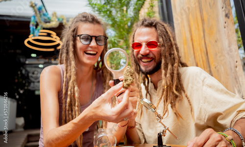 Hippie style couple examines under a magnifying glass the joints and buds of medical marijuana