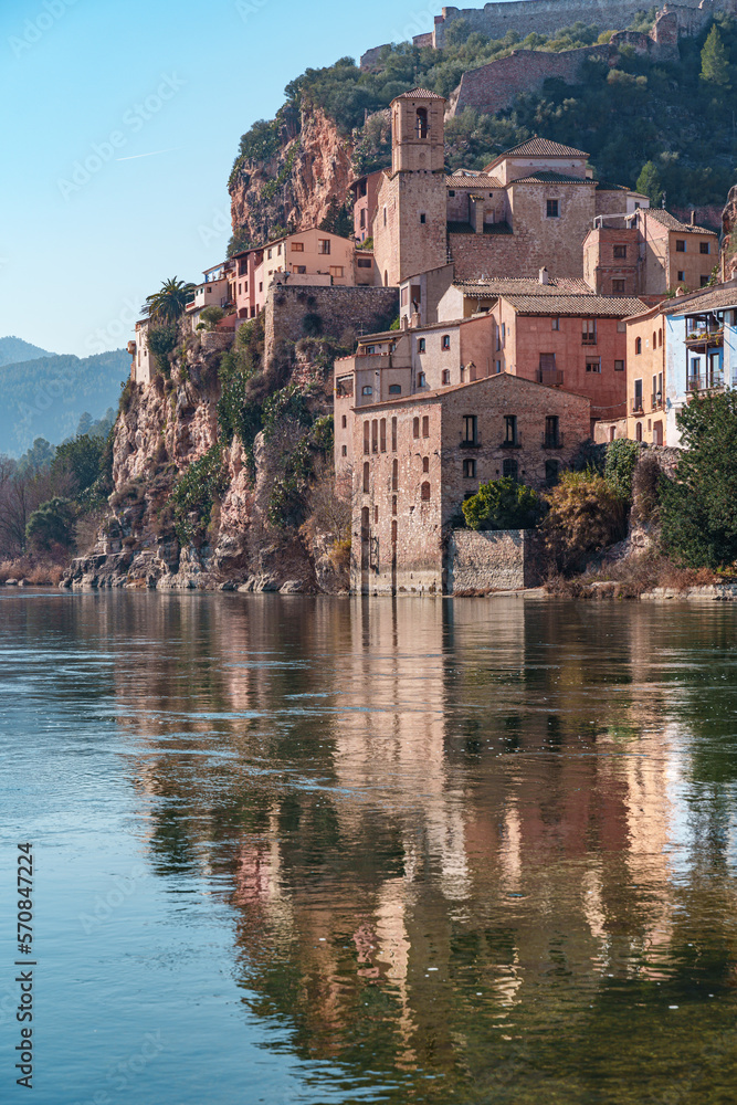 Old town of miravet with the templar castle on the top and the ebro river flowing quietly on a sunny day.