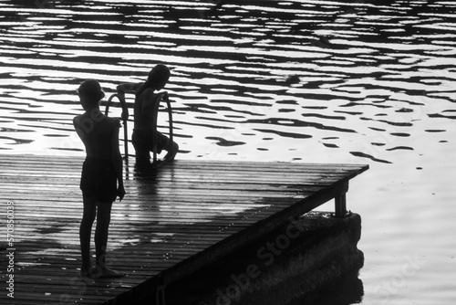 silhouettes d'enfants se baignant depuis un ponton au bord de l'eau le soir en été