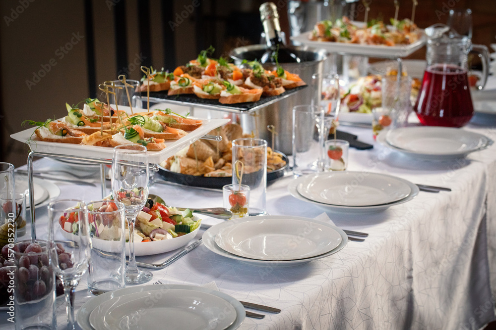 Set table with sandwiches, canapes, salad, wine glasses, plates and a buckets of champagne indoor, selective focus.