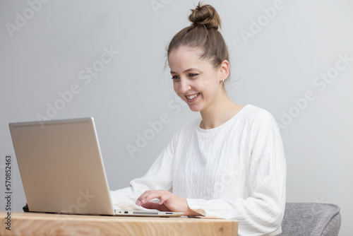 beautiful girl works at home at the table with a laptop in a white sweater on a white background