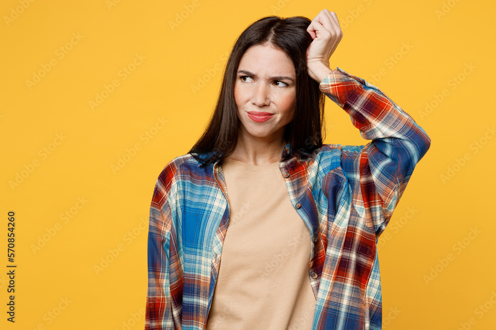 Young sad dissatisfied upset caucasian woman wear blue shirt beige t-shirt look aside on workspace area scratch hold head isolated on plain yellow background studio portrait. People lifestyle concept. Young sad dissatisfied upset caucasian woman wear blue shirt beige t-shirt look aside on workspace area scratch hold head isolated on plain yellow background studio portrait. People lifestyle concept.
