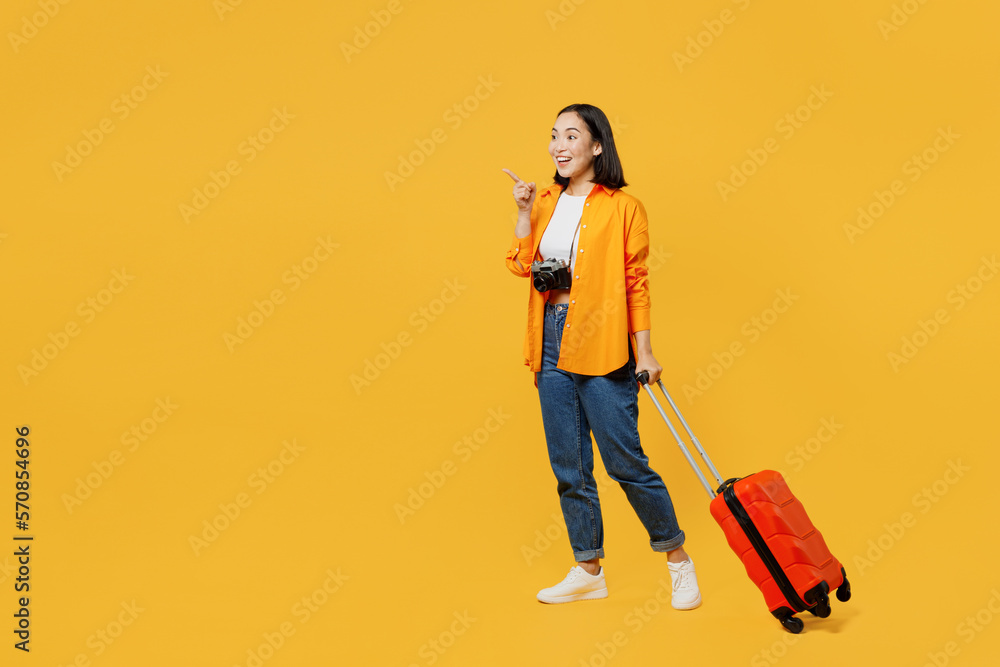Side view young woman wear summer clothes walk go with suitcase point aside isolated on plain yellow background. Tourist travel abroad in free spare time rest getaway. Air flight trip journey concept. Side view young woman wear summer clothes walk go with suitcase point aside isolated on plain yellow background. Tourist travel abroad in free spare time rest getaway. Air flight trip journey concept.