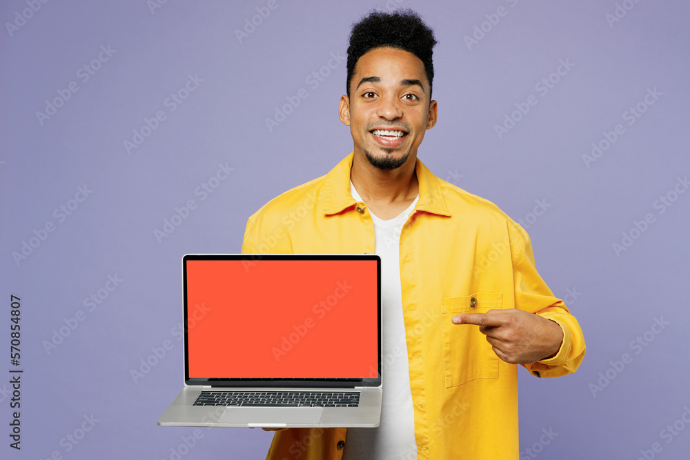 Young IT man of African American ethnicity wear yellow shirt t-shirt hold use work point on laptop pc computer with blank screen workspace area isolated on plain pastel light purple background studio. Young IT man of African American ethnicity wear yellow shirt t-shirt hold use work point on laptop pc computer with blank screen workspace area isolated on plain pastel light purple background studio.