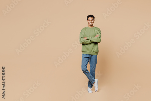 Full body smiling fun young man of African American ethnicity wear green sweatshirt hold hands crossed folded isolated on plain pastel light beige background studio portrait. People lifestyle concept.