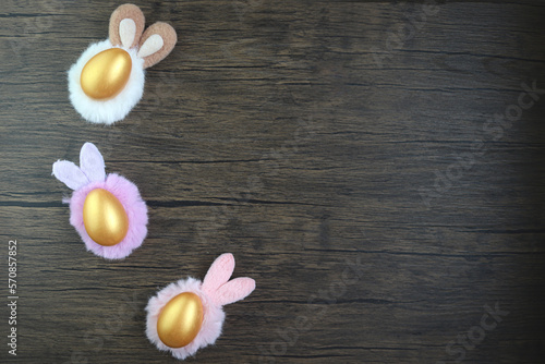 Top view of three beautiful golden Easter eggs wearing bunny rabbit ears headband on rustic brown wooden surface, decoration and celebration Easter and spring beginning.