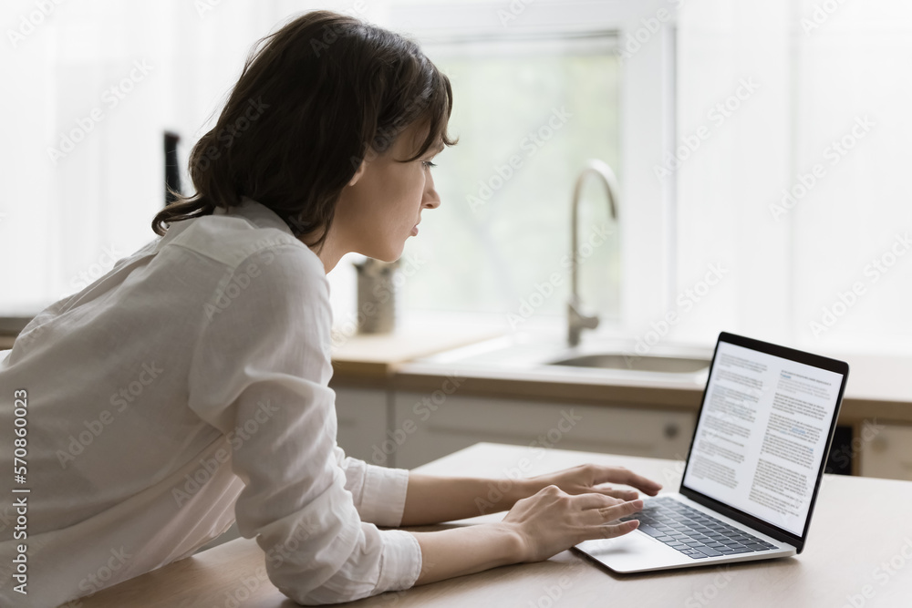 Focused young woman typing on laptop, reading text on screen, monitor. Serious female student, author, blogger creating, editing online article, working on research study