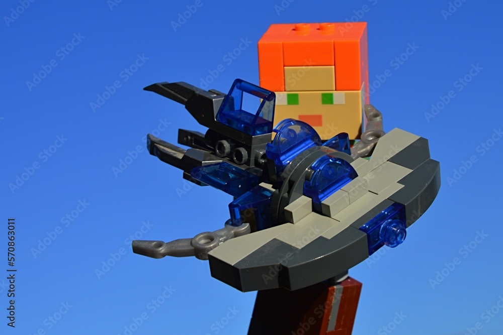 Fototapeta premium LEGO Minecraft figure of Alex holding KREO model of Star Trek Vulcan Jellyfish spaceship, from famous science fiction movie and TV series, known as ship of Mr. Spock. Blue skies in background.
