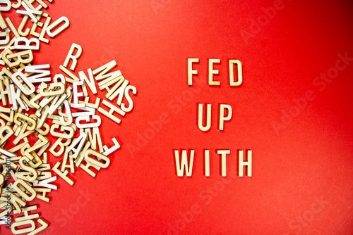 FED UP WITH in wooden English language capital letters spilling from a pile of letters on a red background