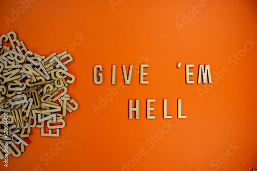 GIVE 'EM HELL in wooden English language capital letters spilling from a pile of letters on a orange background