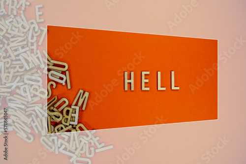 HELL in wooden English language capital letters spilling from a pile of letters on a orange background framed