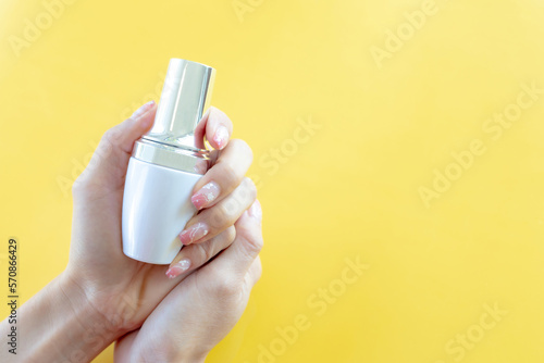 Female s hand holding product of glass bottle with dropper lid on yellow background.Packaging product of cream  lotion  gel  foam or skincare.Cosmetic and medicine product branding mockup.Copy space.